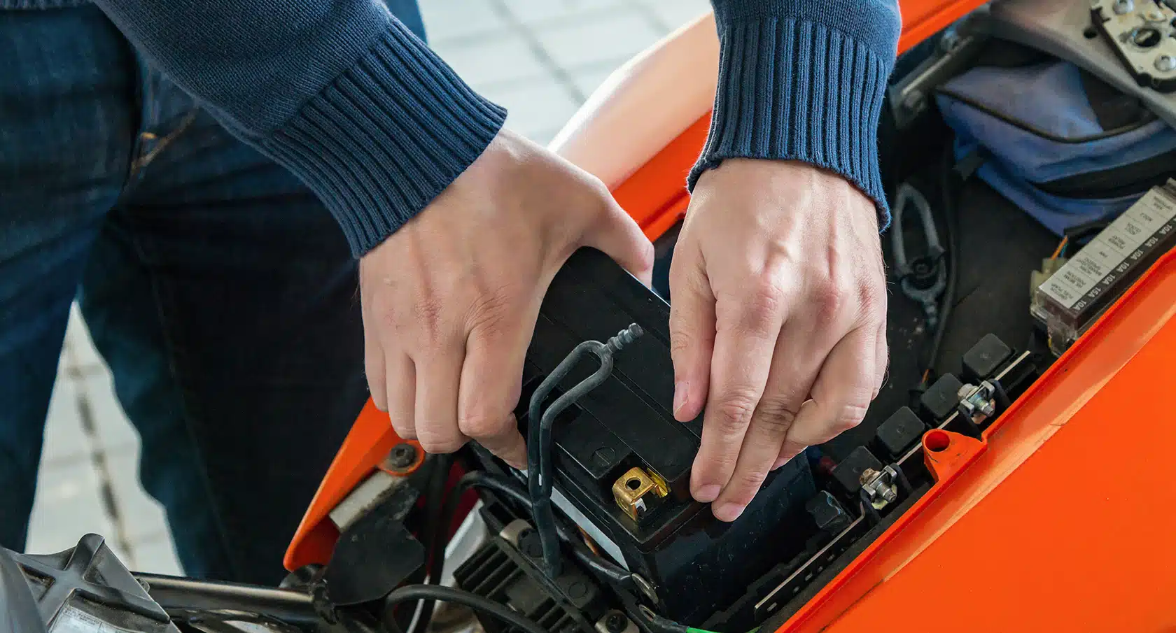 Zwei Hände setzen eine Batterie in ein Motorrad ein