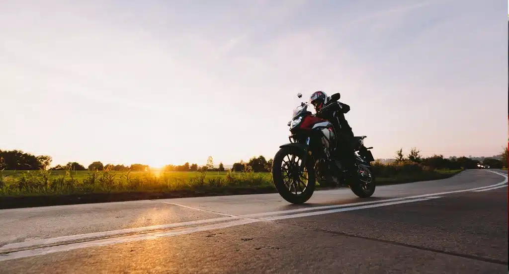 Motorradfahrer fährt auf einer Straße vor Abendsonnenhimmel und Wald