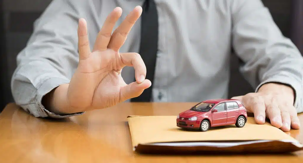 Eine Hand gibt ein positives Zeichen neben einem Briefumschlag und einem Spielzeugauto auf dem Tisch