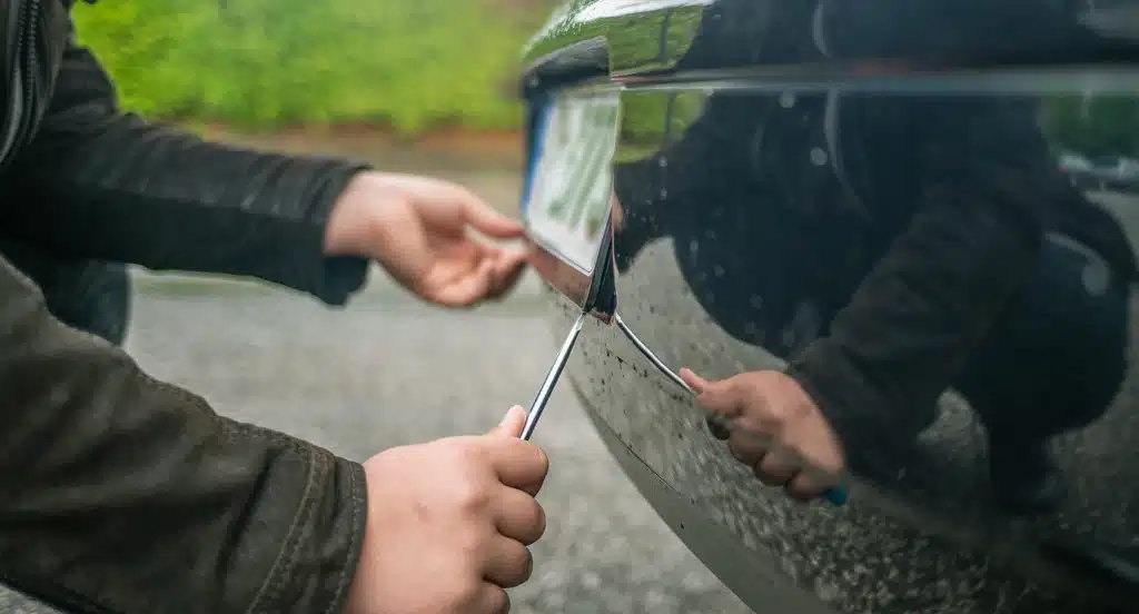 Zwei Hände montieren das Nummernschild eines Autos mithilfe eines Schraubenziehers ab