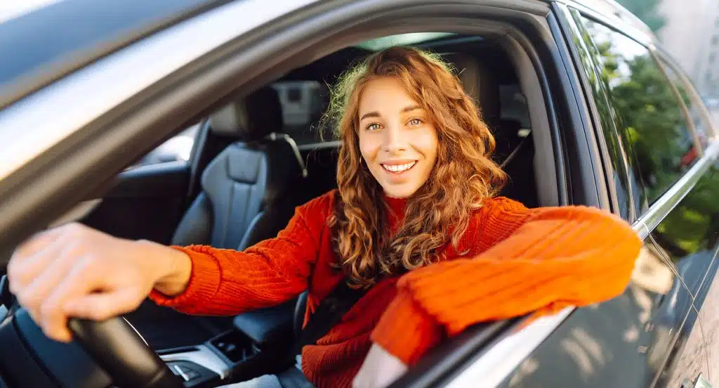Junge Autofahrerin hinterm Steuer eines Autos lehnt lässig ihren Arm aus dem Fenster