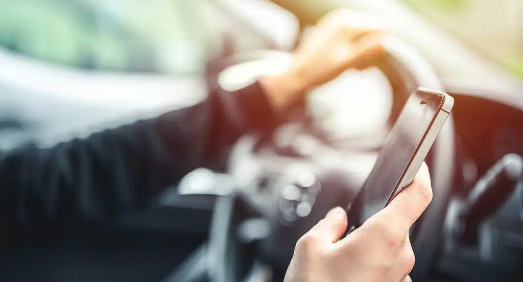 Hand am Steuer eines Autos hält ein Smartphone