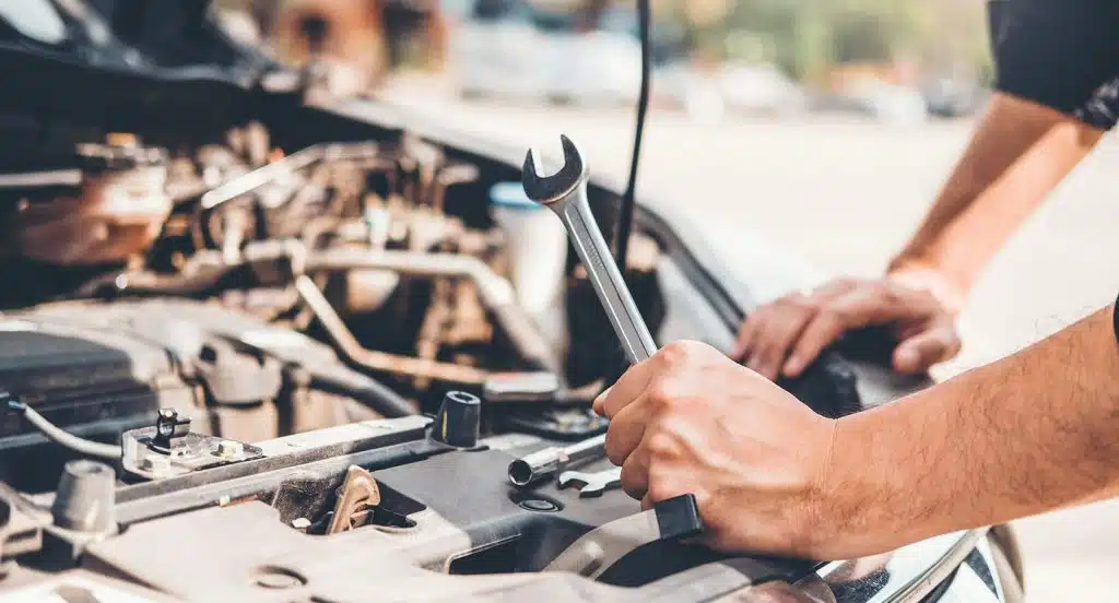 Eine Hand mit einem Schraubschlüssel stützt sich auf einen Motorblock einer geöffneten Autohaube