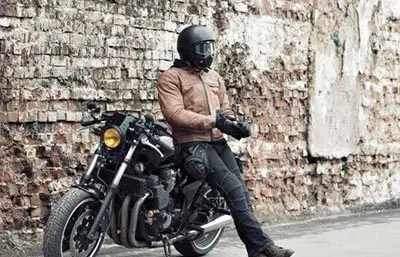 Motorradfahrer mit schwarzem Helm lehnt mit dem Rücken an einem Motorrad
