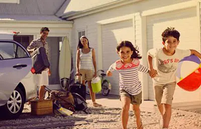 Familie im Urlaub. Eltern stehen mit Gepäck am Auto und Kinder rennen mit Ball zum Strand