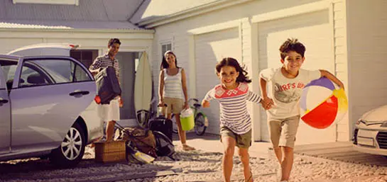 Familie im Urlaub. Eltern stehen mit Gepäck am Auto und Kinder rennen mit Ball zum Strand